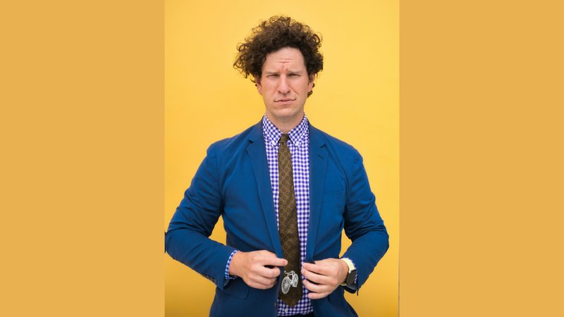 Colorado appellate attorney Daniel H. Kyser raising a skeptical eyebrow in a blue blazer and patterned tie against a yellow background