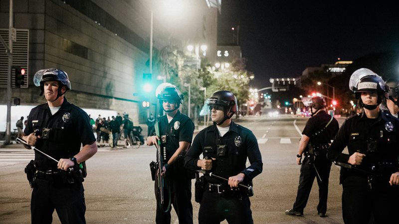 Line of police officers in riot helmets holding batons on a city street at night