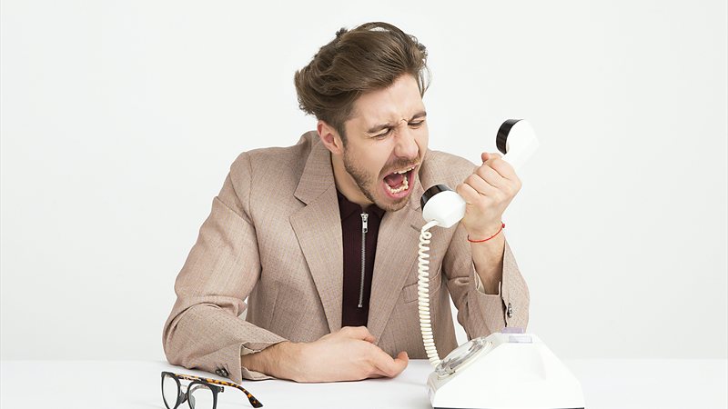 Angry man in a blazer shouting into a retro telephone handset