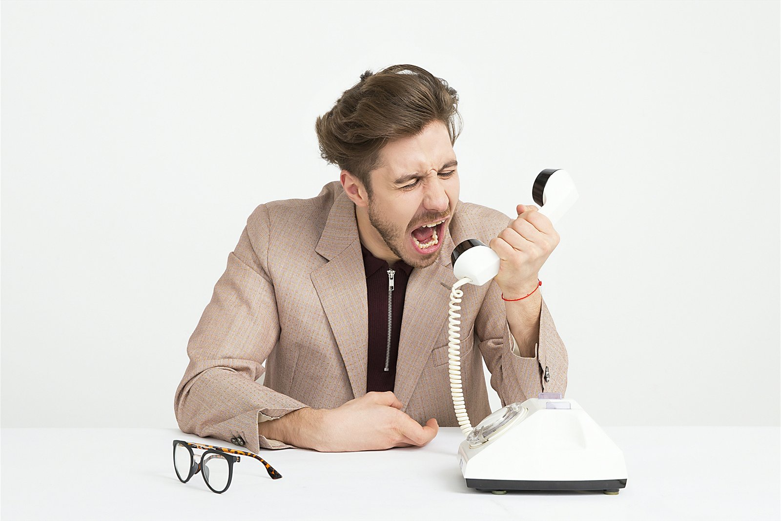 Angry man in a blazer shouting into a retro telephone handset against a white background